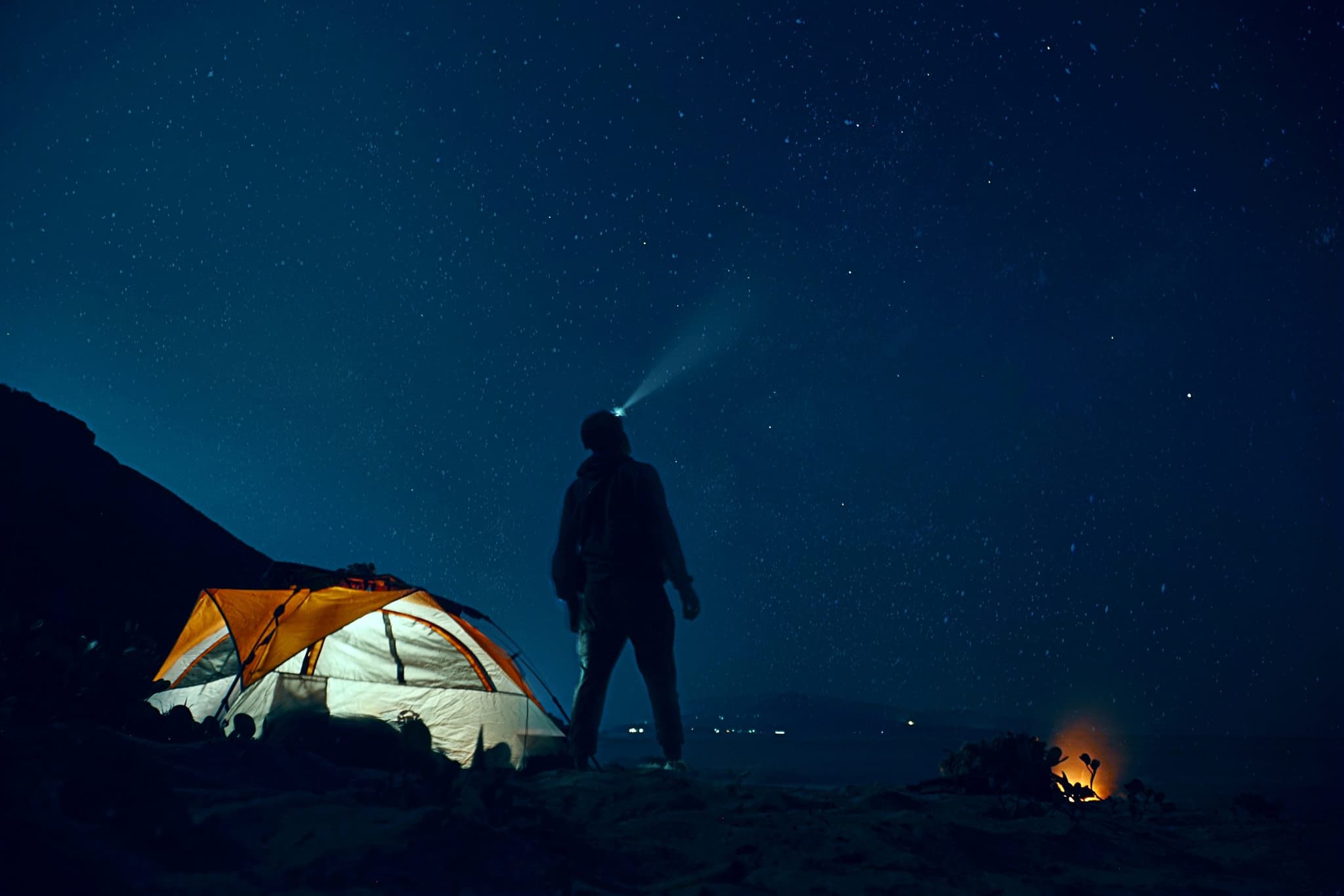 A hiker and illuminated tent beneath the stars